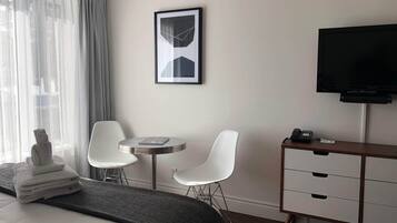 Een hotelkamer met een bed, een bureau met stoelen, een televisie en een lijst met een afbeelding aan de muur.