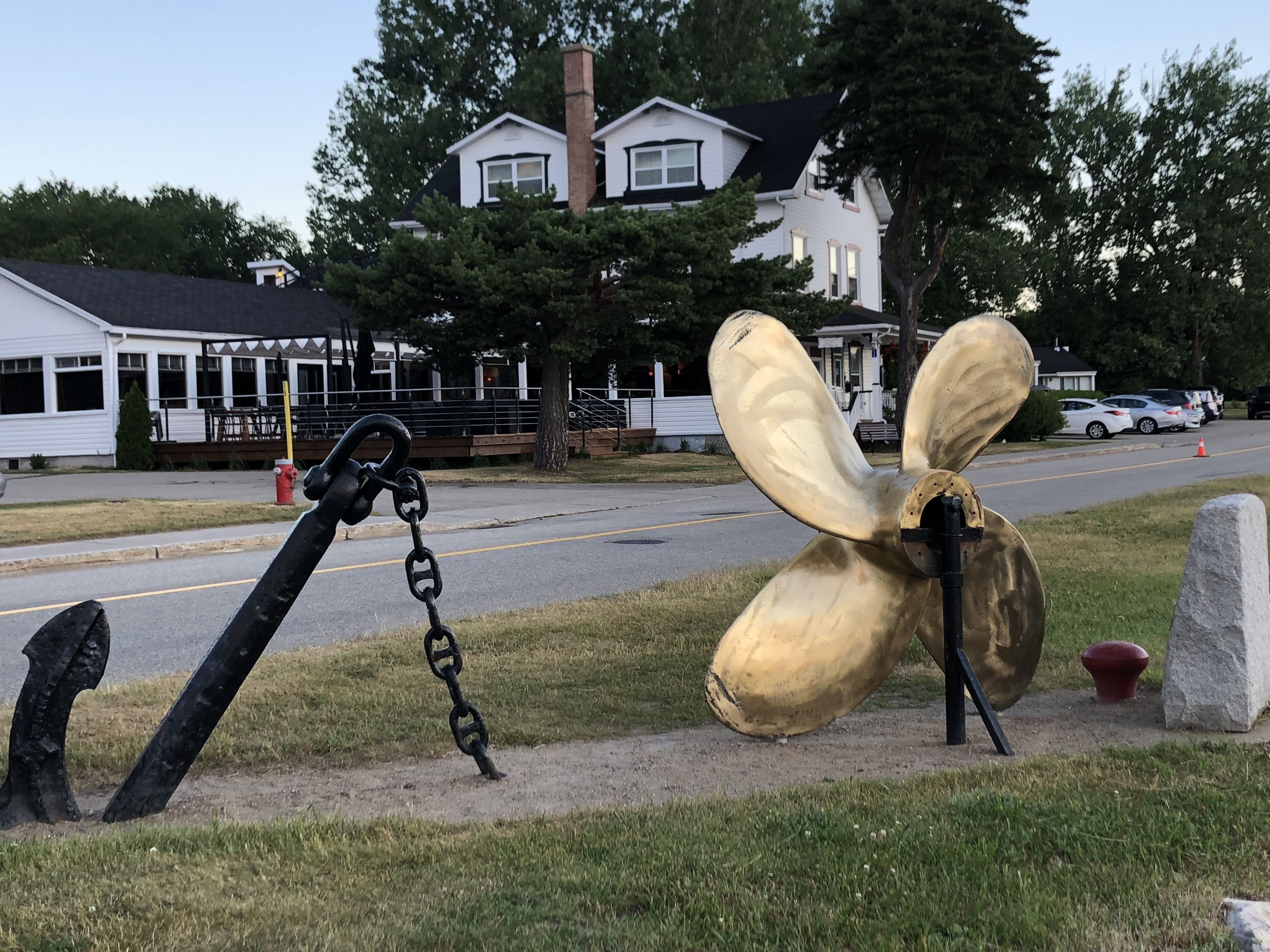 A large anchor sculpture on a grassy area near a road with a building in the background.