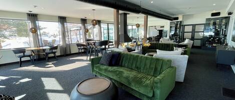 A modern hotel lobby with a green sofa, round coffee table, and dining area with chairs and tables.