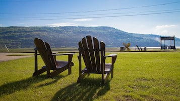 Relax in a serene outdoor setting with Adirondack chairs on a lush lawn overlooking a tranquil hillside and a nearby marina.