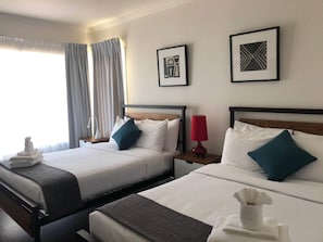 Een hotelkamer met twee bedden, een nachtkastje met een lamp, en kunst aan de muur.