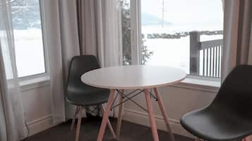 A room with a round table and two chairs, large windows with curtains, and a view of a snowy landscape.
