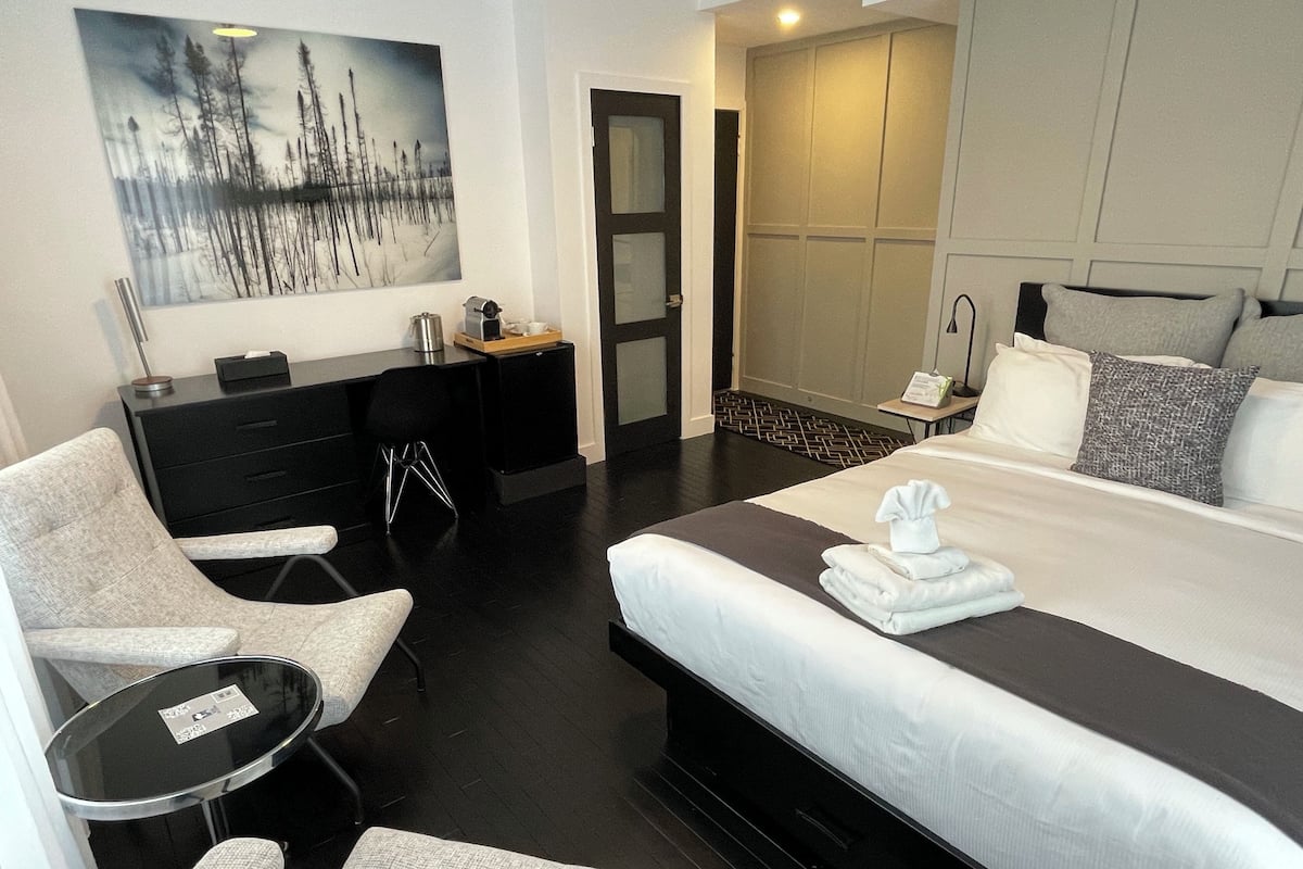 A modern hotel room with a large bed, a desk, a chair, and a small table.