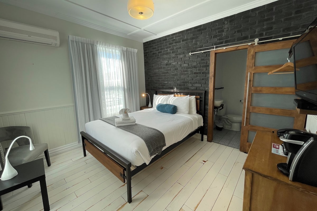 A modern hotel room with a bed, a desk, a chair, a wardrobe, and a bathroom.