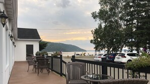 Une terrasse en bois, meublée de meubles en osier, offrant une vue sur l’eau et les montagnes.