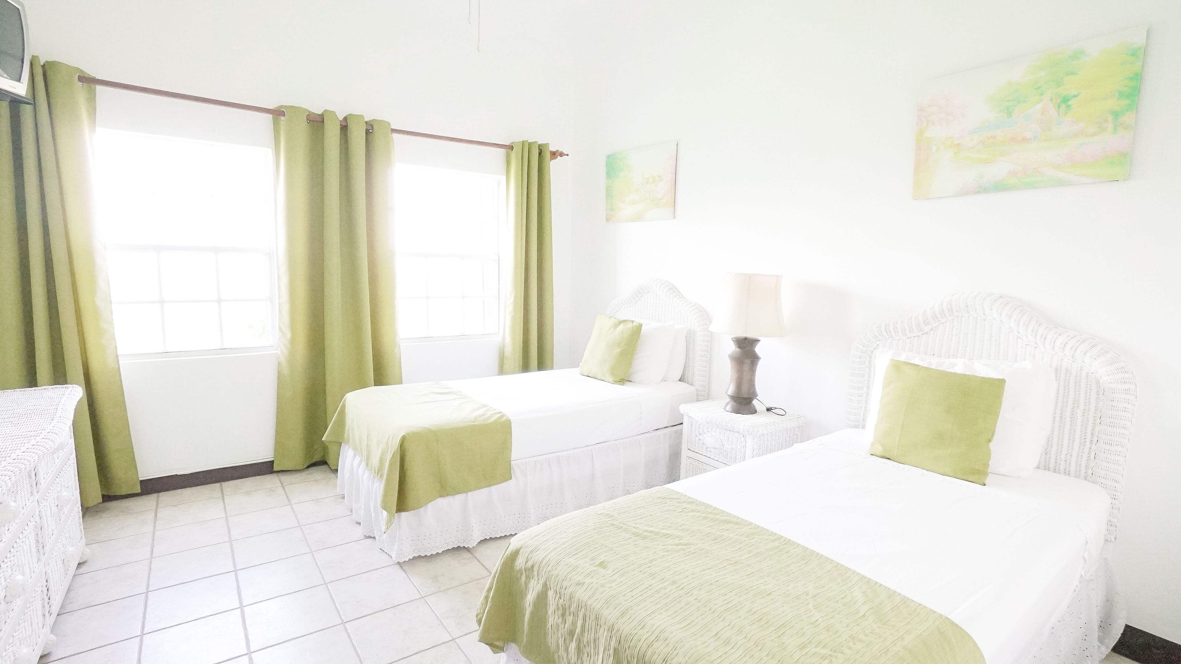 Una habitación de hotel con dos camas, una mesita de noche con lámpara y una ventana con cortinas.