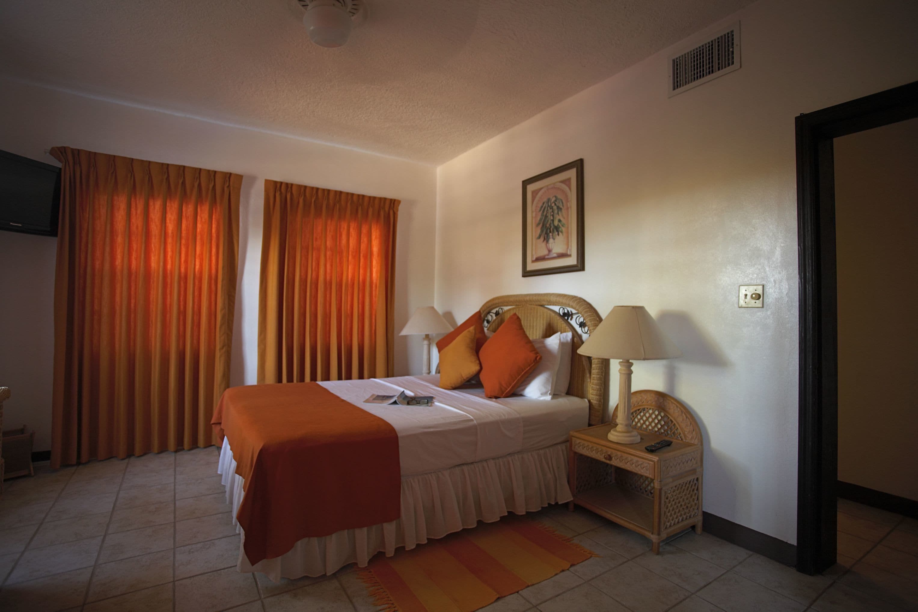 Una habitación de hotel con cama, mesita de noche, lámpara, televisor y cortinas.