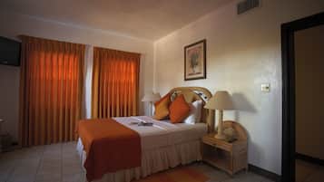 A hotel room with a bed, a nightstand, a lamp, a television, and curtains.