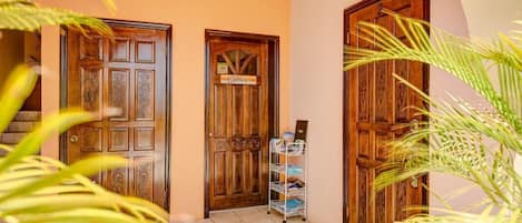 Un pasillo con dos puertas de madera, una que indica “Office” y la otra con un letrero encima. Una estantería metálica con revistas está colocada contra la pared.