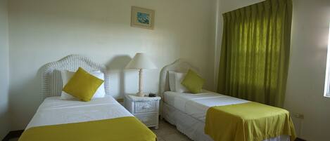 A hotel room with two beds, each with a white headboard and a yellow bedspread. There is a small bedside table with a lamp and a picture on the wall above it.