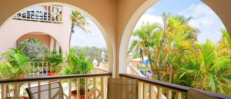 A balcony with a round table and chairs, surrounded by potted plants and palm trees.