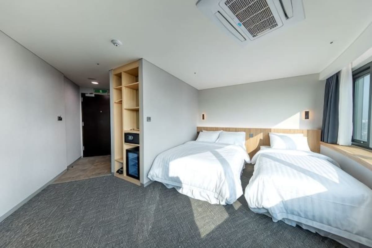 A hotel room with two beds, a built-in wardrobe, and a large window.