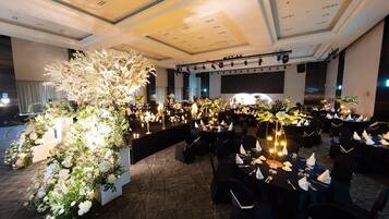 Un salón de banquetes con mesas dispuestas para un evento formal, destacando centros de mesa florales y un escenario con equipo de iluminación.