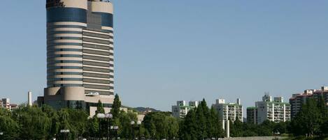 A tall, modern building with horizontal windows, surrounded by greenery and a body of water.