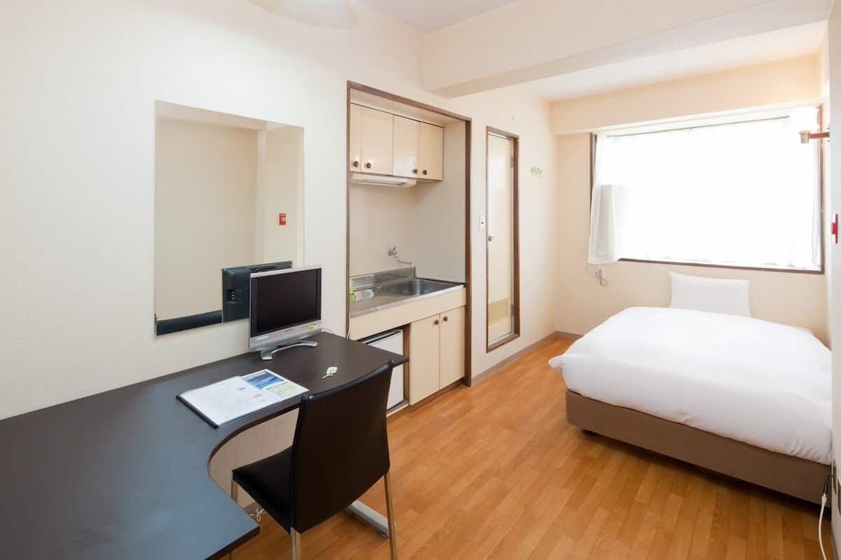 A hotel room with a bed, a desk with a computer, a small kitchenette, and a window.