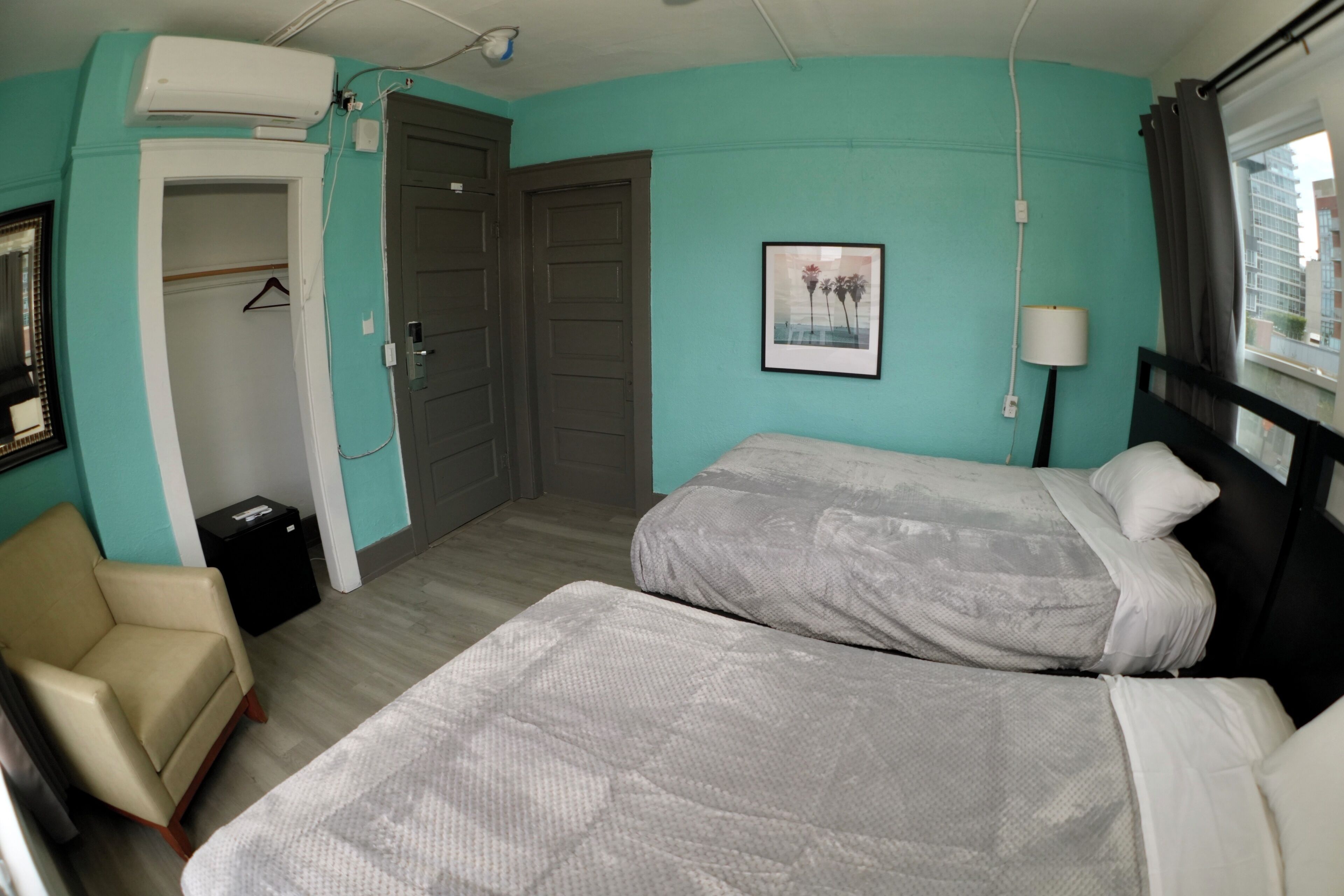 A room with two beds, a chair, a wardrobe, and a picture on the wall.