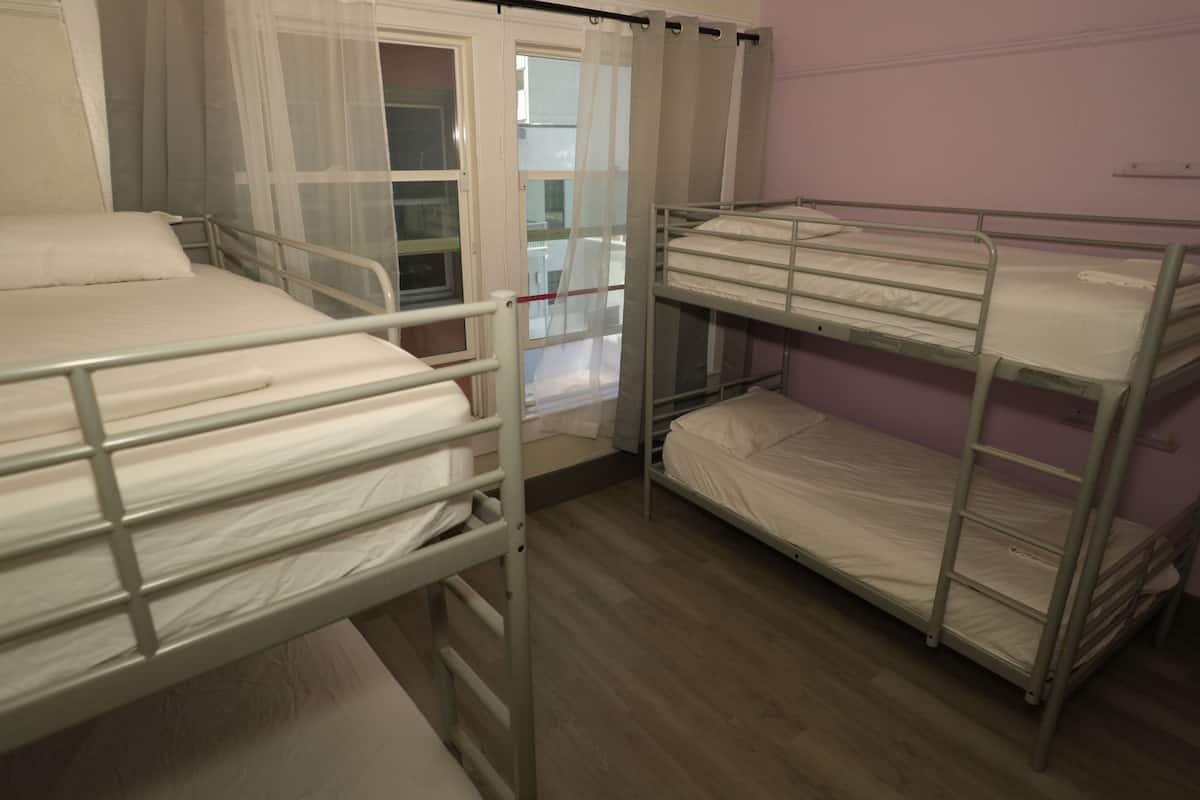 A room with bunk beds, a window with sheer curtains, and a door leading to another room.