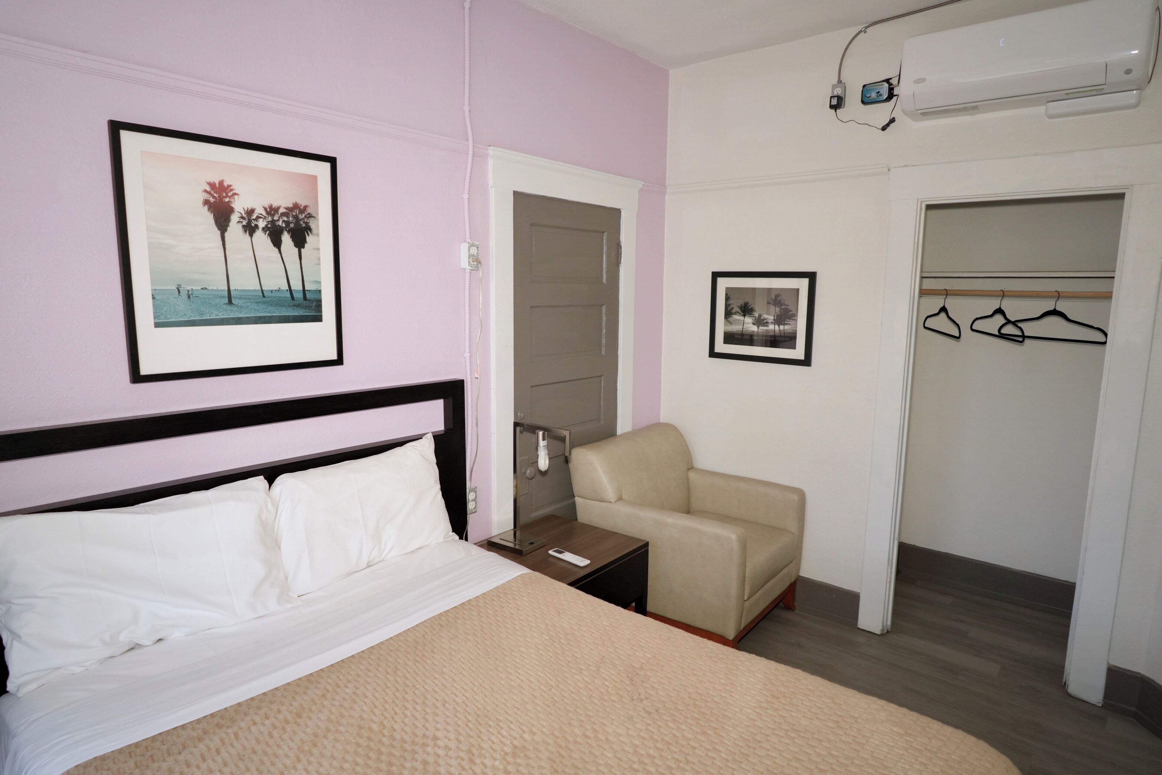 A hotel room with a bed, a chair, a wardrobe, and two framed pictures on the wall.