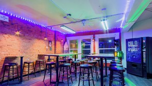 Eine Barbereich mit Barhocker, einer Theke, einem Deckenventilator und einem Automaten mit der Aufschrift 'COLD drinks'.