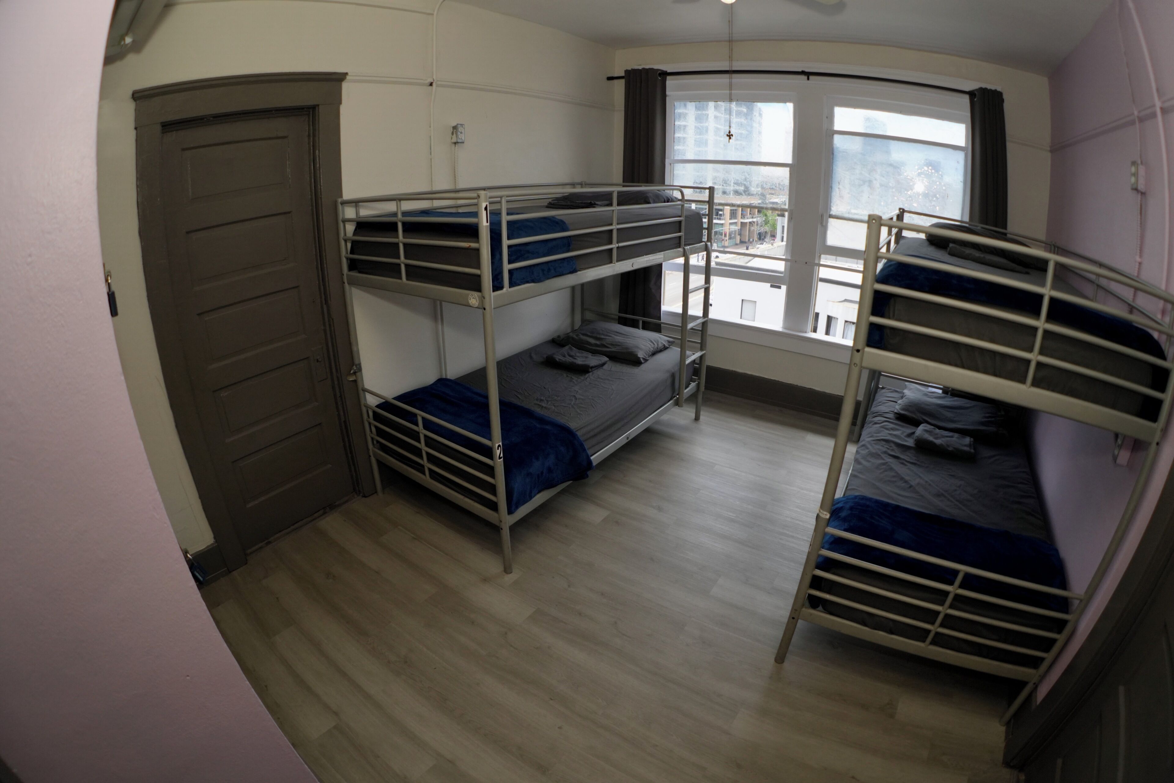 A dormitory room with bunk beds, a door, and a window.
