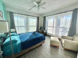 A modern hotel room with a large bed, a desk, a chair, and a ceiling fan.