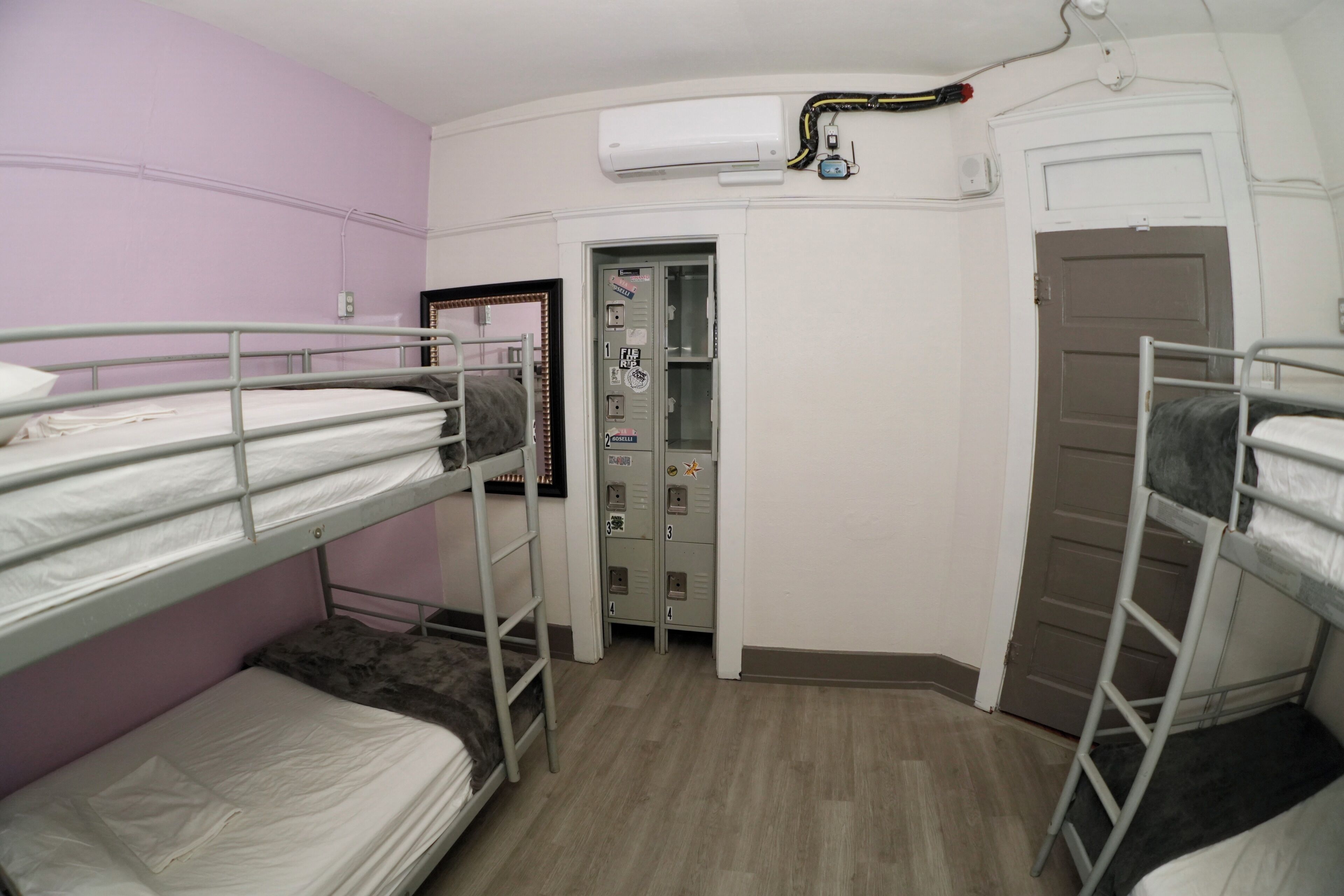 A dormitory room with bunk beds, a door, a wall-mounted air conditioner, and a doorbell.