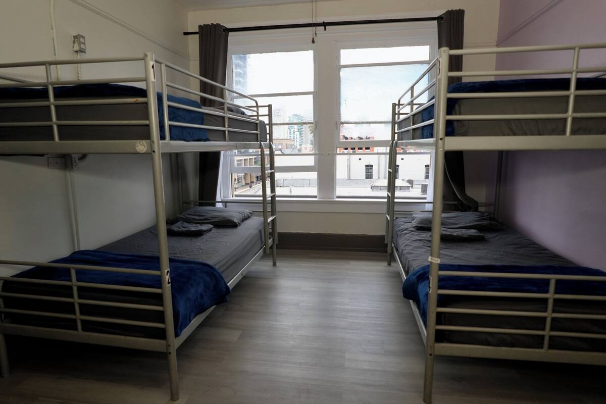 A room with bunk beds, a window, and a view of buildings outside.
