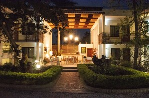 A well-lit outdoor area with a covered seating area, a pathway leading to the entrance, and a building with multiple balconies. - Maxime Boutique Hotel (Petionville)