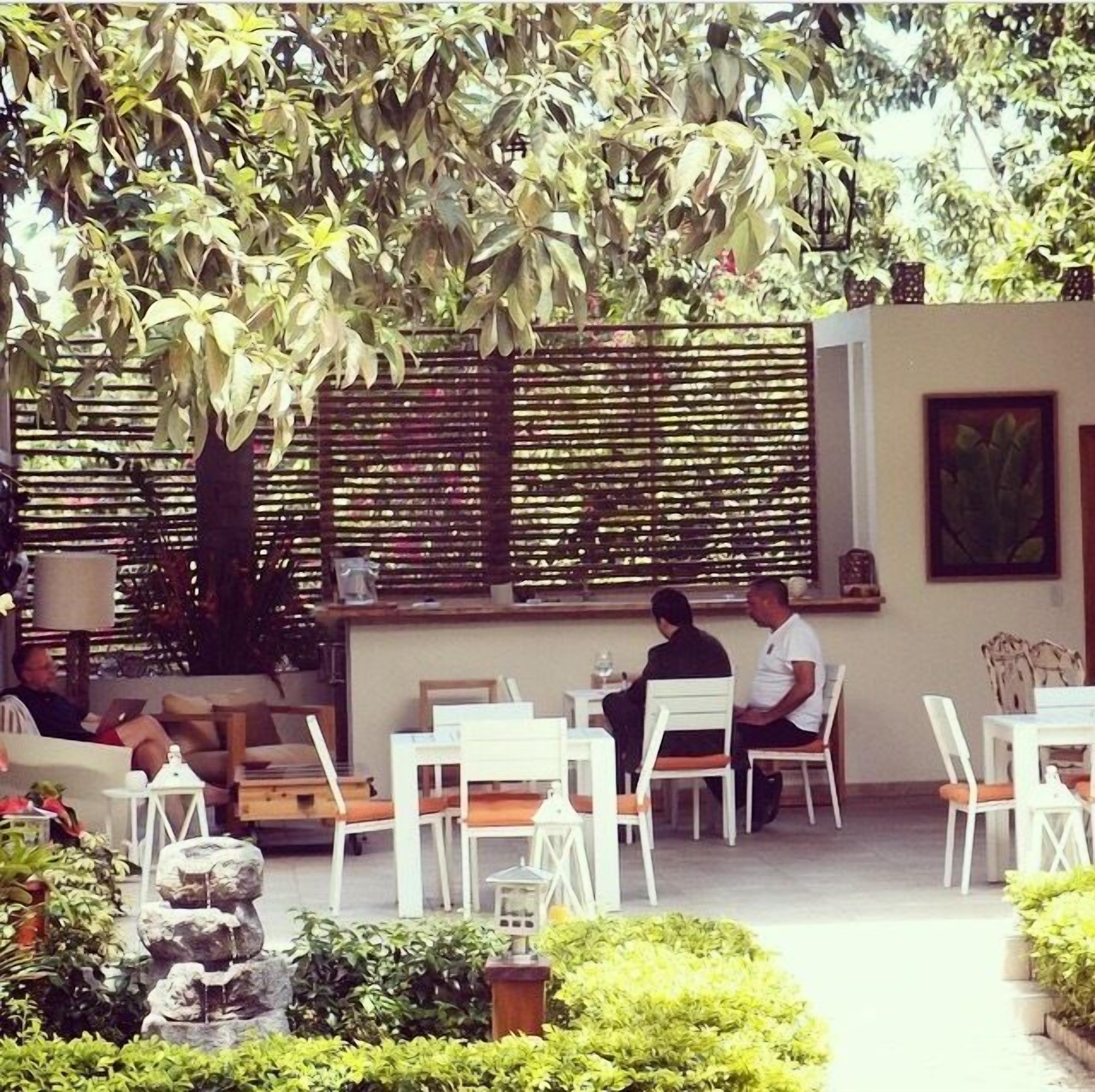 Area pranzo all'aperto con tavoli e sedie, una recinzione in legno e vegetazione.