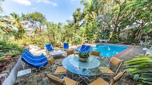 Un espace aménagé au bord de la piscine, avec une table en verre entourée de chaises, une petite piscine et une végétation luxuriante.