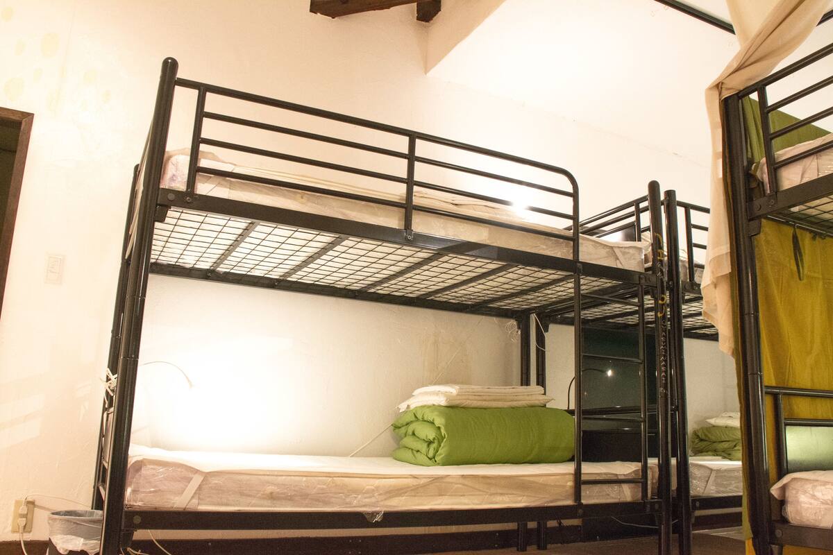 Habitación con literas de estructura metálica, un colchón y una manta verde.