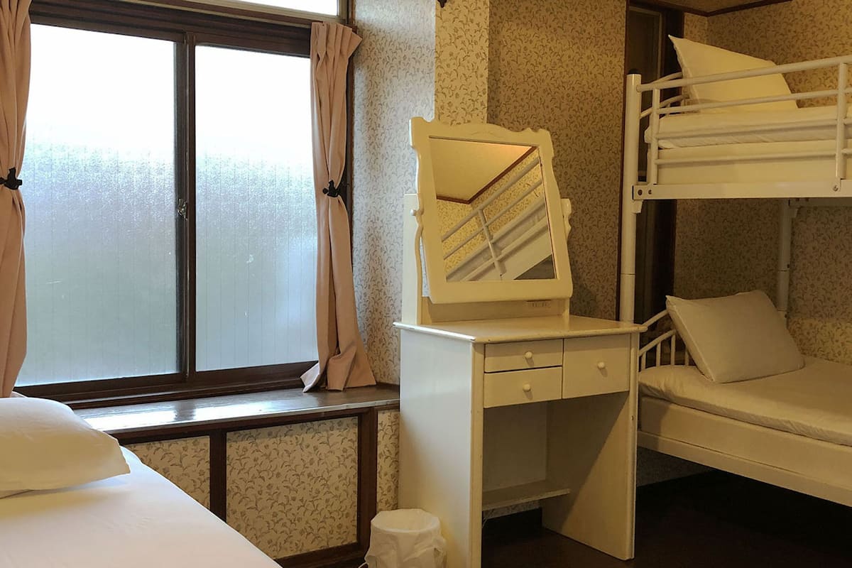 Un dormitorio con literas, una ventana, un escritorio con cajones y un espejo.
