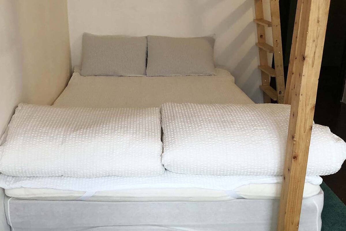 Una cama individual con escalera de madera, ropa de cama blanca y una alfombra verde.