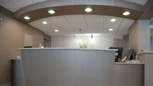 A reception area with a curved counter, ceiling lights, and a potted plant. - Brentwood Inn & Suites (Rochester)