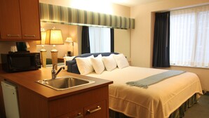 A hotel room with a bed, a sink, a microwave, and a window with curtains. - Brentwood Inn & Suites (Rochester)