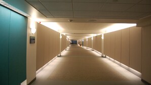 A long, narrow hotel corridor with a carpeted floor, light fixtures along the walls, and a ceiling with recessed lighting. - Brentwood Inn & Suites (Rochester)