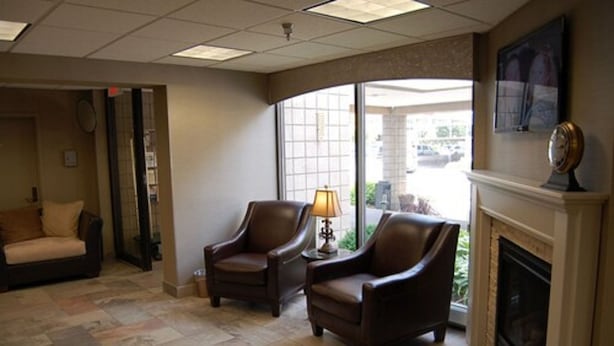 A room with a fireplace, two leather armchairs, a sofa, and a large window providing a view of the outdoors. - Brentwood Inn & Suites (Rochester)