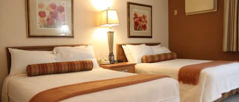 Quarto de hotel com duas camas, uma mesa de cabeceira, uma luminária e quadros com flores nas paredes.
