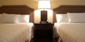 A hotel room with two beds, each with white bedding and a headboard. There is a nightstand between the beds with a lamp and a telephone. - Brentwood Inn & Suites (Rochester)