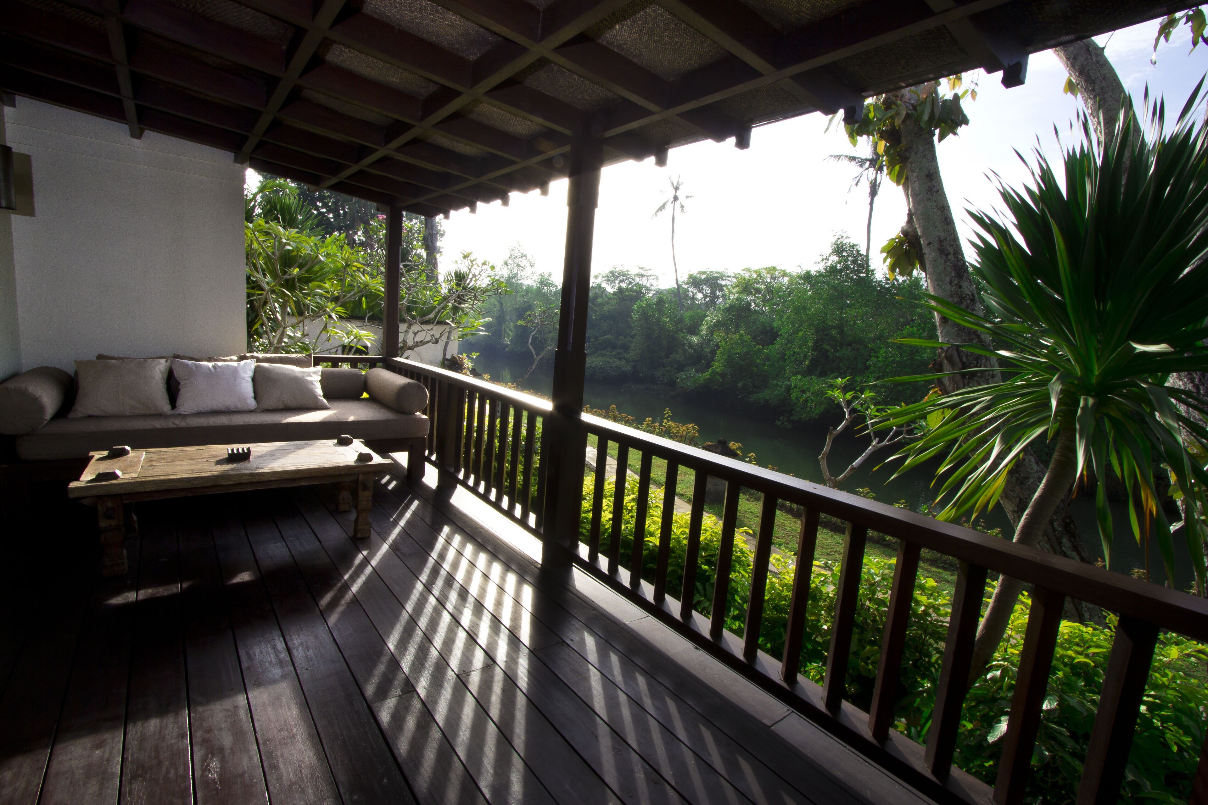 A wooden deck with a sofa and a table, overlooking a lush green landscape with trees and a river.