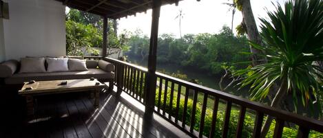 A wooden deck with a sofa and a table, overlooking a lush green landscape with trees and a river.
