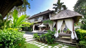Ein tropisches Resort mit Pool, überdachter Lounge-Ecke und üppiger Bepflanzung.