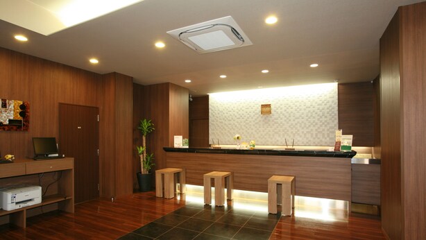 A modern reception area with a wooden desk, a printer, and a potted plant. - Hotel Route Inn Ishinomaki Chuo (Isinomaki)