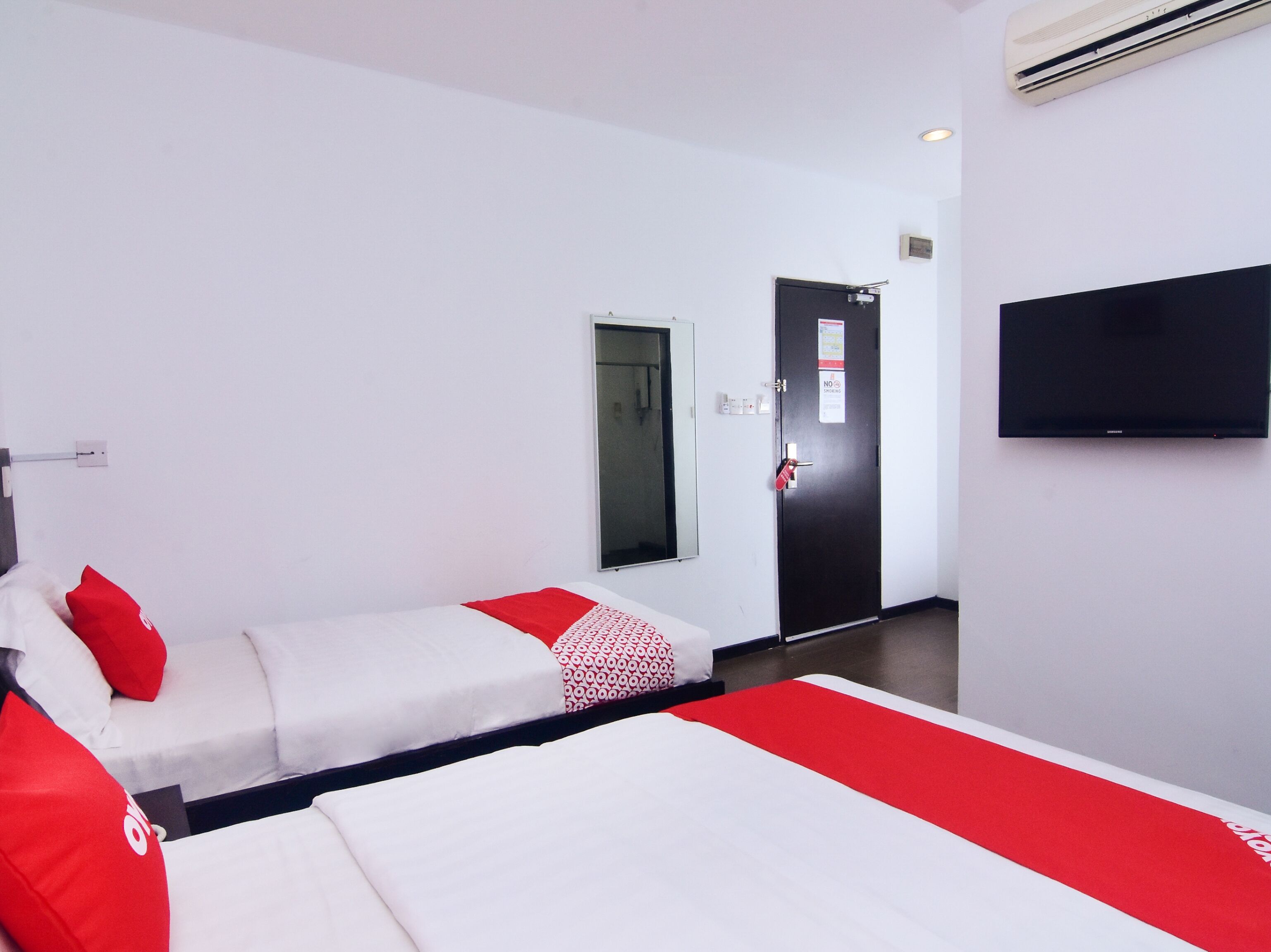 A hotel room with a bed, a sofa, a TV, and a door with a sign.