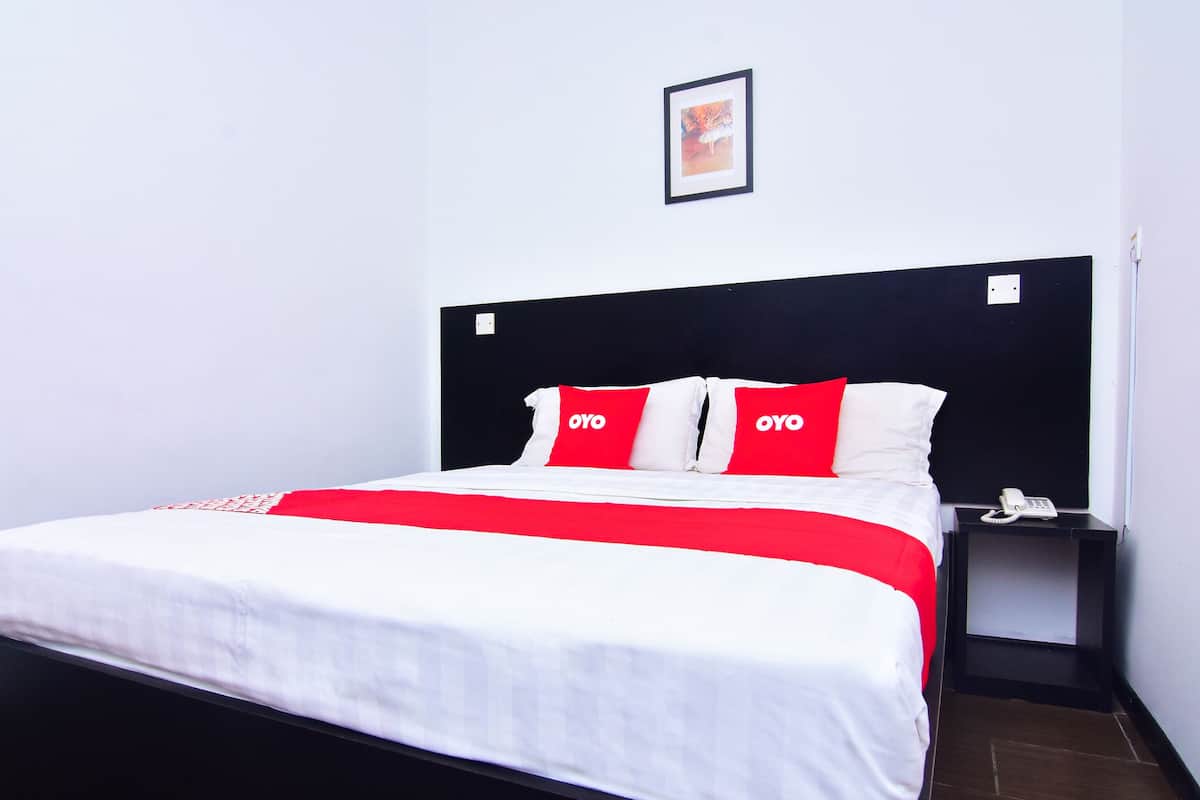 Habitación de hotel con cabecera negra, ropa de cama blanca y almohadas rojas y blancas con la palabra 'OYO'.