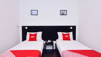 A hotel room with two beds, each with a red OYO pillow, a bedside table with a phone, and two framed pictures on the wall.