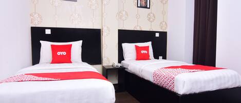 Two single beds with black headboards and white bedding, each with a red pillow and a red and white patterned throw.
