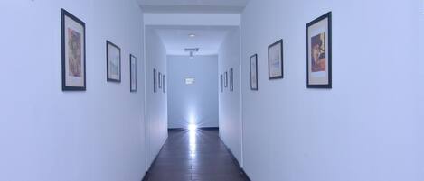 A hallway with framed pictures on the walls, a sign indicating room number 129, and a ceiling light.