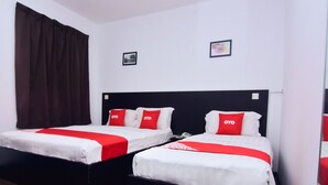 A hotel room with two beds, each with a black headboard and white bedding. There are red pillows with the logo "OYO" on them. The room has a brown curtain on one side and a white wall with two framed pictures.