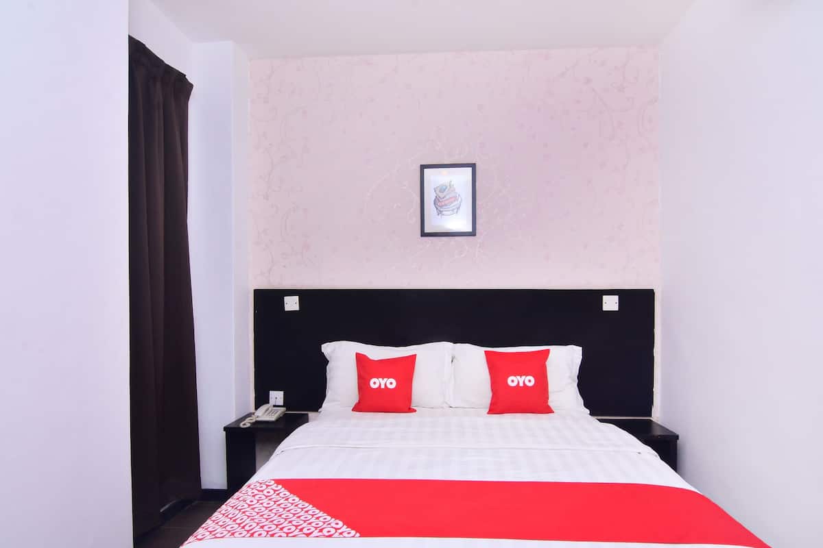 Habitación de hotel con una cama, dos almohadas con la marca 'OYO', una mesita de noche con un teléfono y un cuadro en la pared.